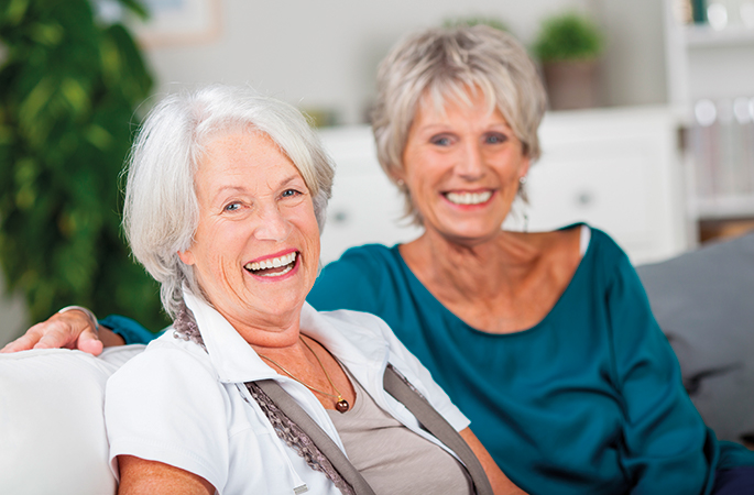 Två äldre kvinnor sitter i en soffa och skrattar