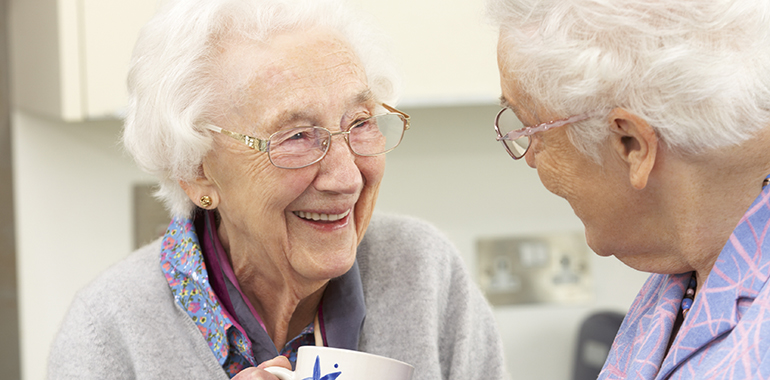 Två äldre kvinnor som ler och pratar med varandra