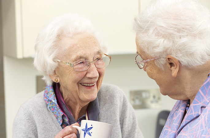 Två äldre kvinnor som ler och pratar med varandra